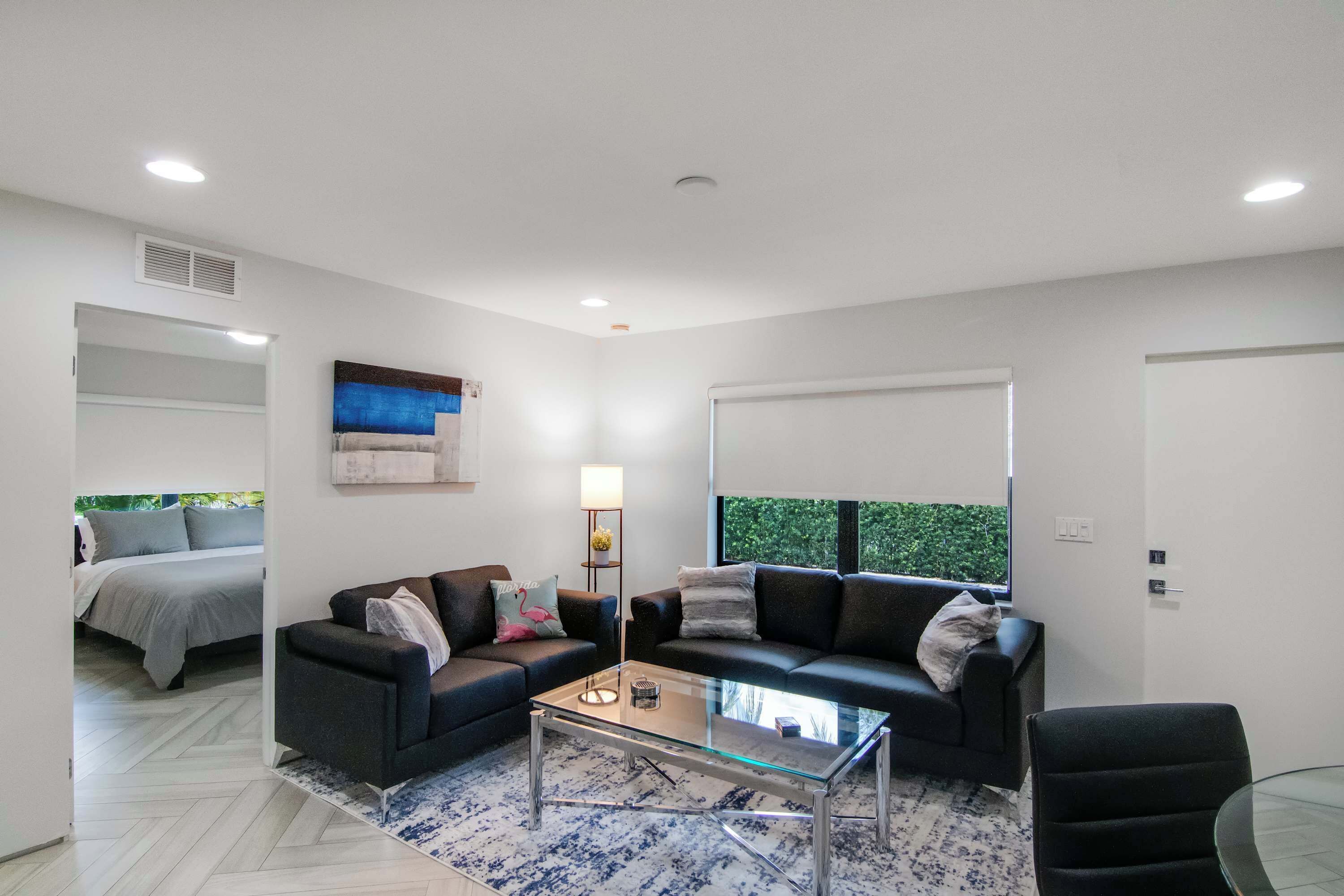A modern living room with a glass coffee table, two sofas, a lamp, and a view of greenery outside.