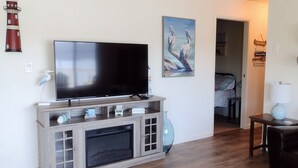 Een woonkamer met een flatscreen televisie, een open haard, een bank en een deur naar een slaapkamer.