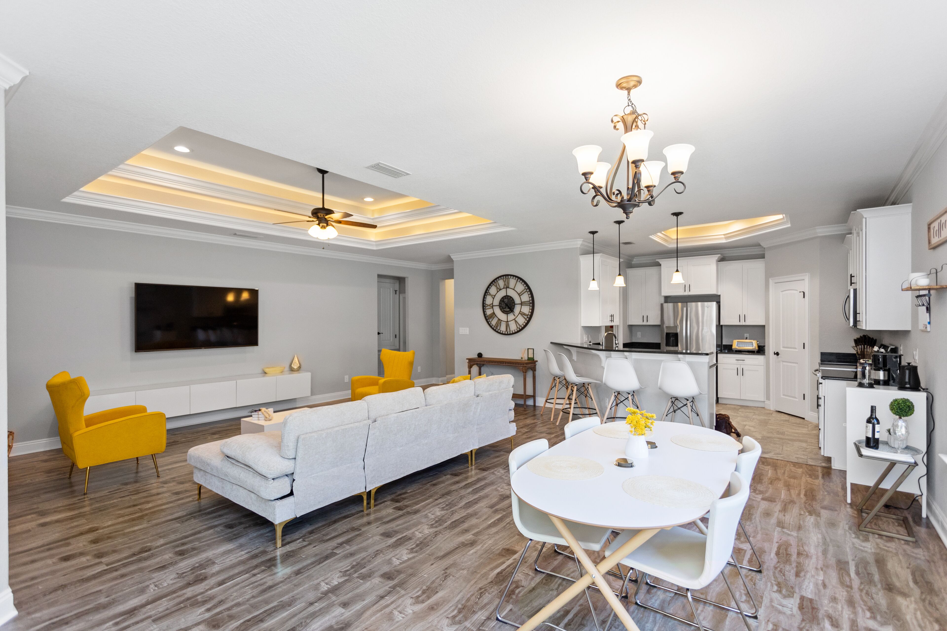 A modern living room with a sofa, yellow chairs, a dining table, and a kitchen area with cabinets and a TV.