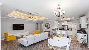 Una sala de estar moderna con un sofá, sillas amarillas, una mesa de comedor y una cocina con armarios y un televisor.