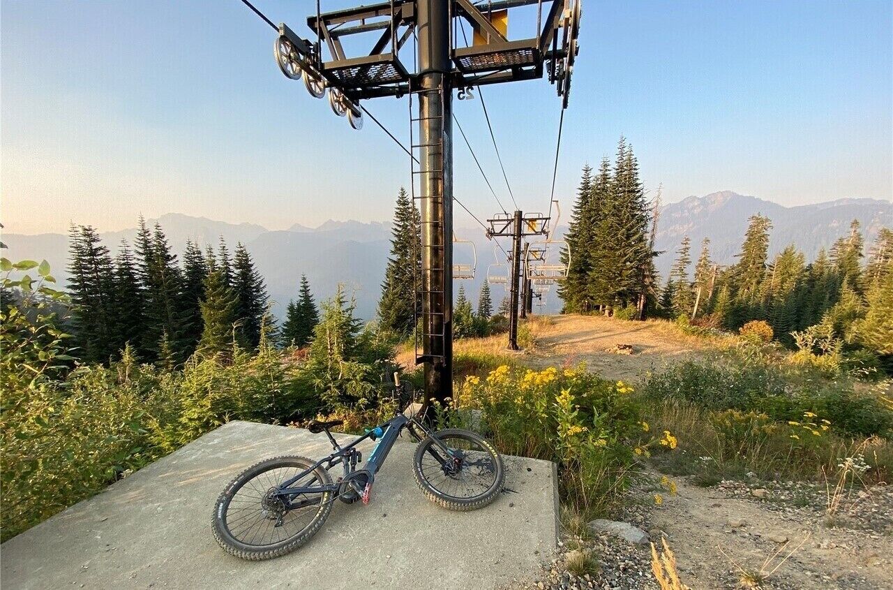 Una bicicleta de montaña aparcada sobre una losa de hormigón con un telesilla y una montaña boscosa al fondo.