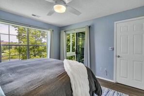 A bedroom with a bed, a ceiling fan, a window, and a door.