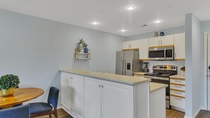 A modern kitchen with white cabinets, a built-in microwave, a refrigerator, and a dining area with a wooden table and chairs. - Enclosed Patio! Golf-Course View Near Branson Strip (Branson)