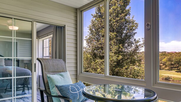 A balcony with a glass table, a cushioned chair, and a view of a tree and landscape. - Enclosed Patio! Golf-Course View Near Branson Strip (Branson)