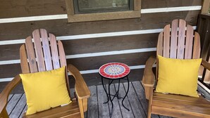 Dos sillas Adirondack de madera con cojines amarillos en una terraza de madera con una mesita redonda.