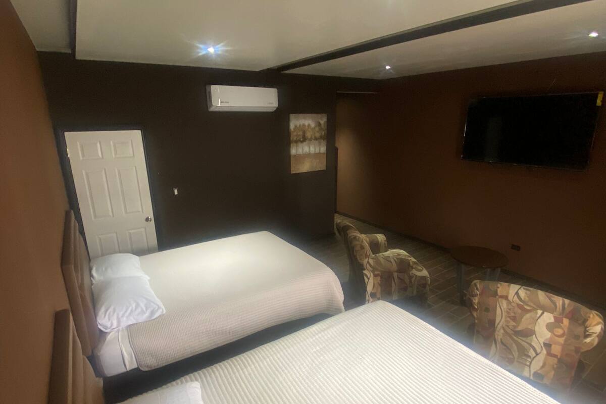 Une chambre d’hôtel avec deux lits, un canapé, une télévision et un appareil de climatisation.