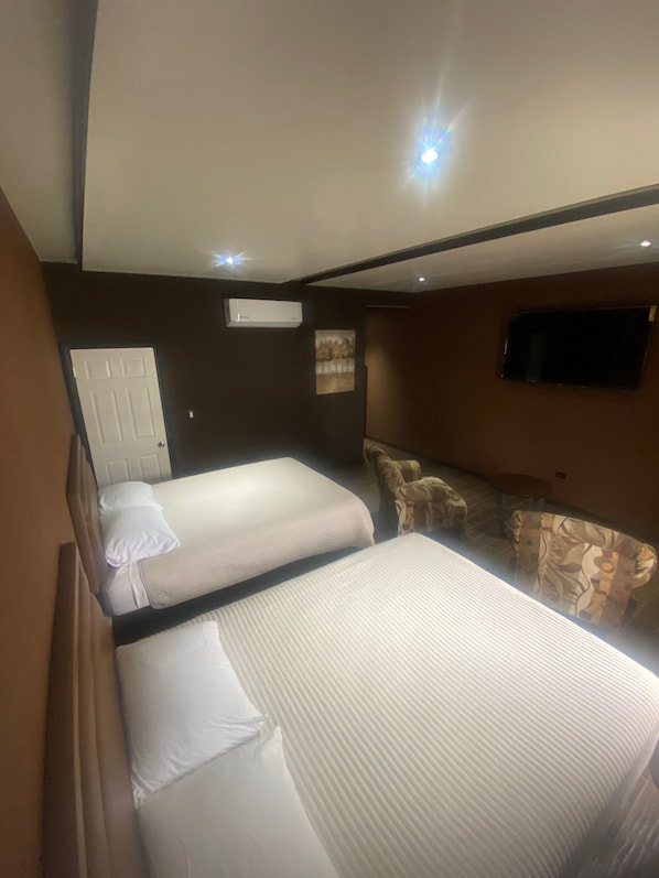 A hotel room with two beds, a sofa, a TV, and an air conditioning unit. - Hotel Pedregal (Nogales)