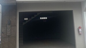 En bygning med stor garageindgang, brandslukker og et lille vindue med gardin.