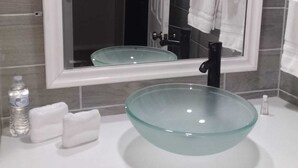 Et badeværelse med en skålformet vask i glas, hvide håndklæder og et spejl, der reflekterer rummet.