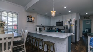 Una cocina moderna con armarios blancos, una isla grande con taburetes, un microondas y un refrigerador.