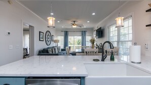 Una cocina moderna con encimera de mármol, lavavajillas integrado y una isla grande. Hay una zona de comedor con mesa y sillas, y un ventilador de techo.