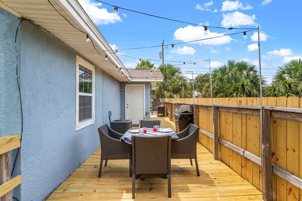 A covered patio with a table and chairs, a wooden deck, and a wooden fence.