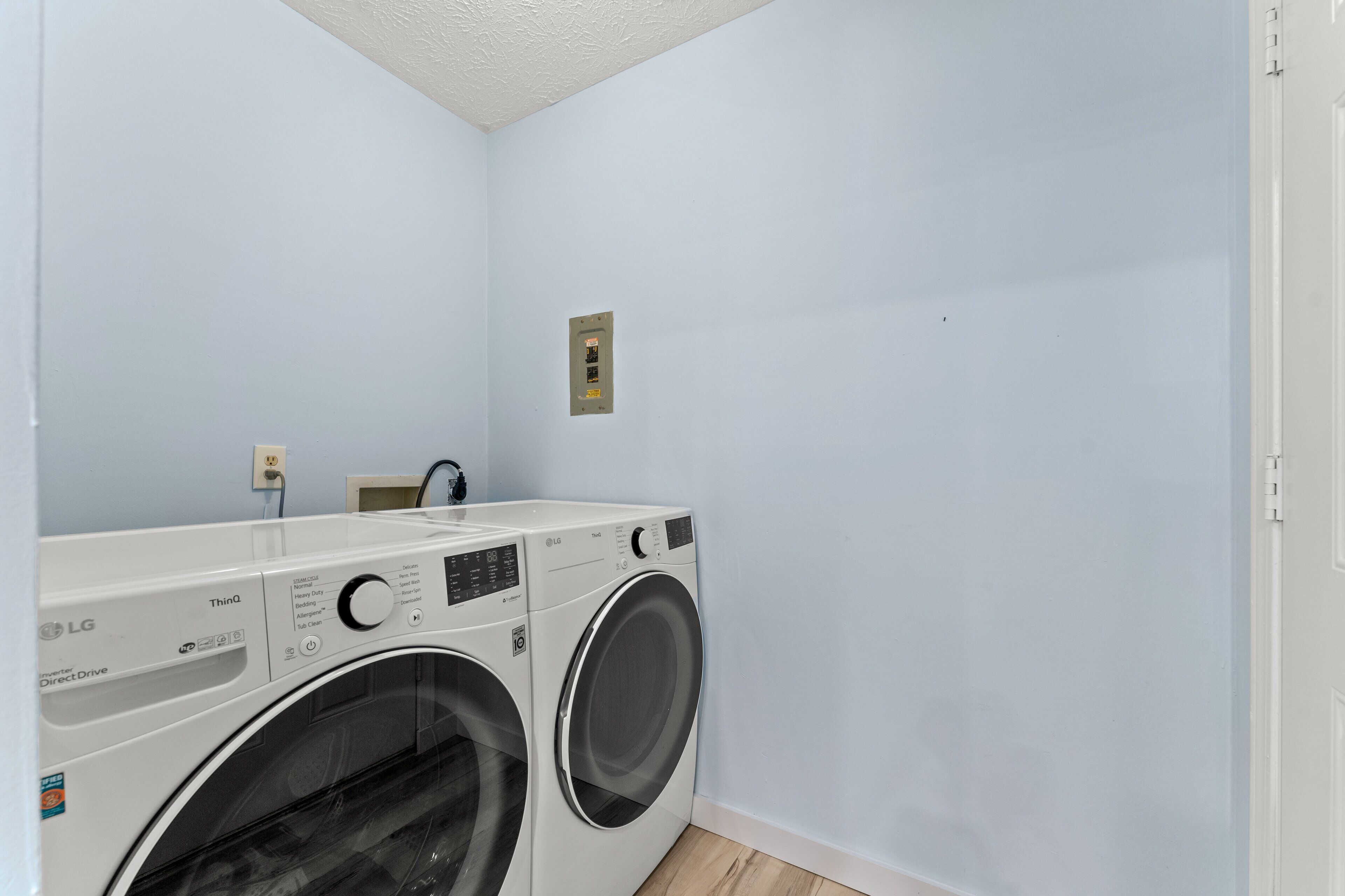 A laundry room with two front-loading LG washers and dryers, a power outlet, and a light switch on the wall.