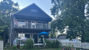 A two-story house with a balcony, a small porch with a blue umbrella, and a flag. - Lovely waterfront 2 bedroom apartment (New Franklin)
