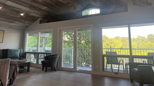 A spacious room with a high ceiling, large windows, and a balcony with outdoor furniture. - Lovely waterfront 2 bedroom apartment (New Franklin)