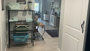 A hallway with a black metal rack holding folded towels, a welcome sign, and a door leading to a kitchen area. - Lovely waterfront 2 bedroom apartment (New Franklin)