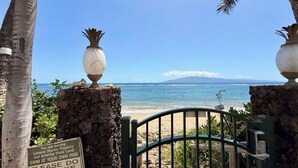 A beach gate with a warning sign, palm trees, and a clear view of the ocean and a distant mountain. - Legal STR Hotel Zoned Lahaina Shores Serene Beachfront Escape with Mountain View (Lahaina)