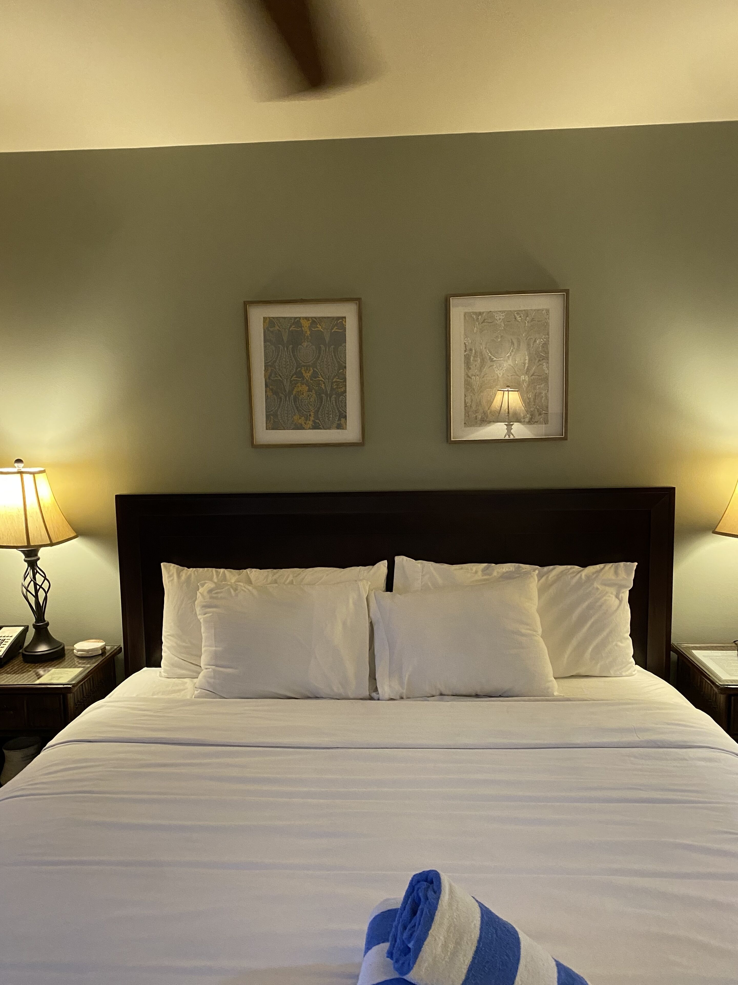 A hotel room with a large bed, two framed artworks on the wall, and two bedside lamps.