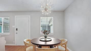 A dining area with a round table, four wooden chairs, a potted plant, and a modern ceiling light fixture.