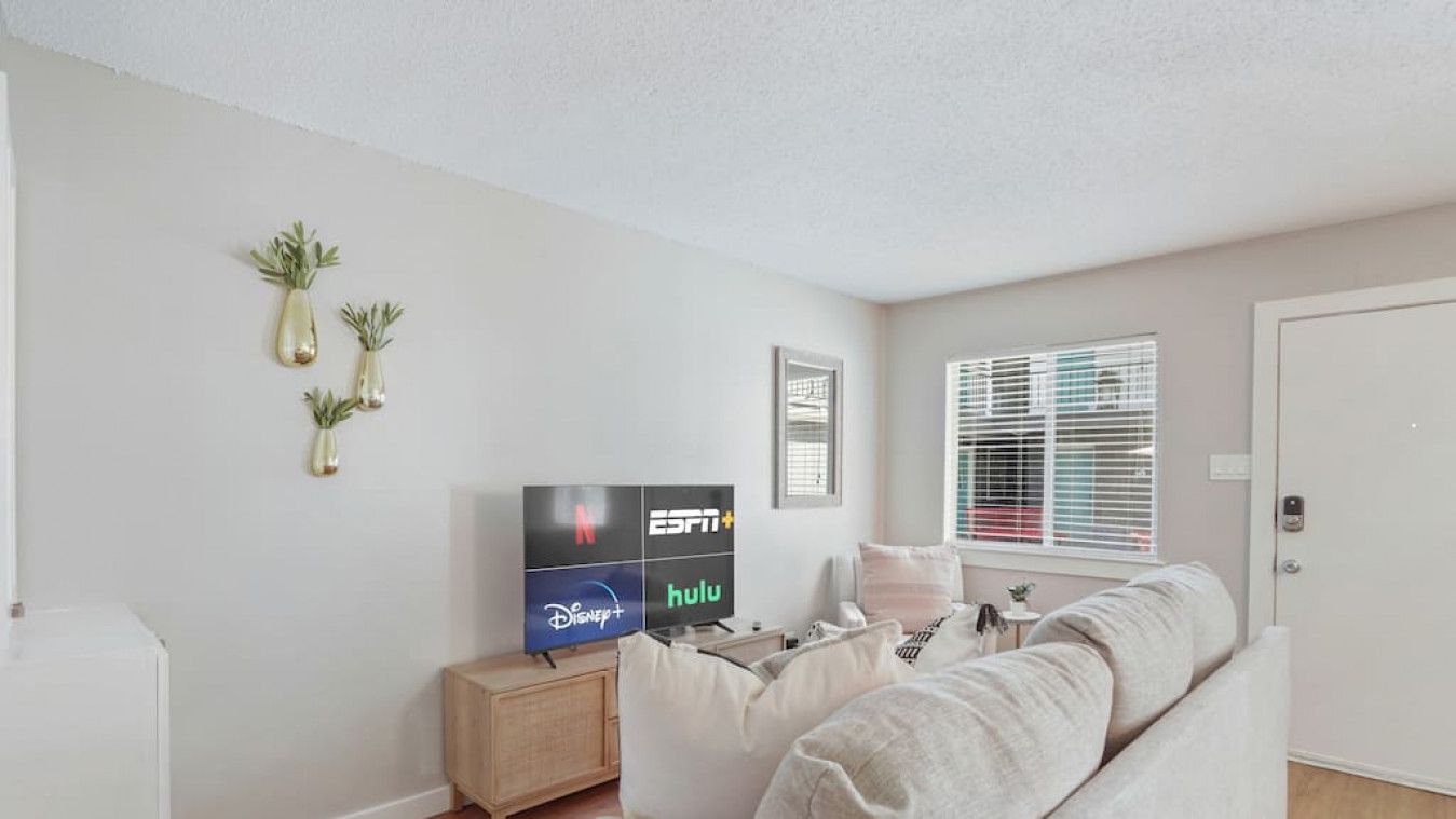 Een moderne woonkamer met een bank, een televisie waarop logo's van streamingdiensten staan, en een klein houten bijzettafeltje.
