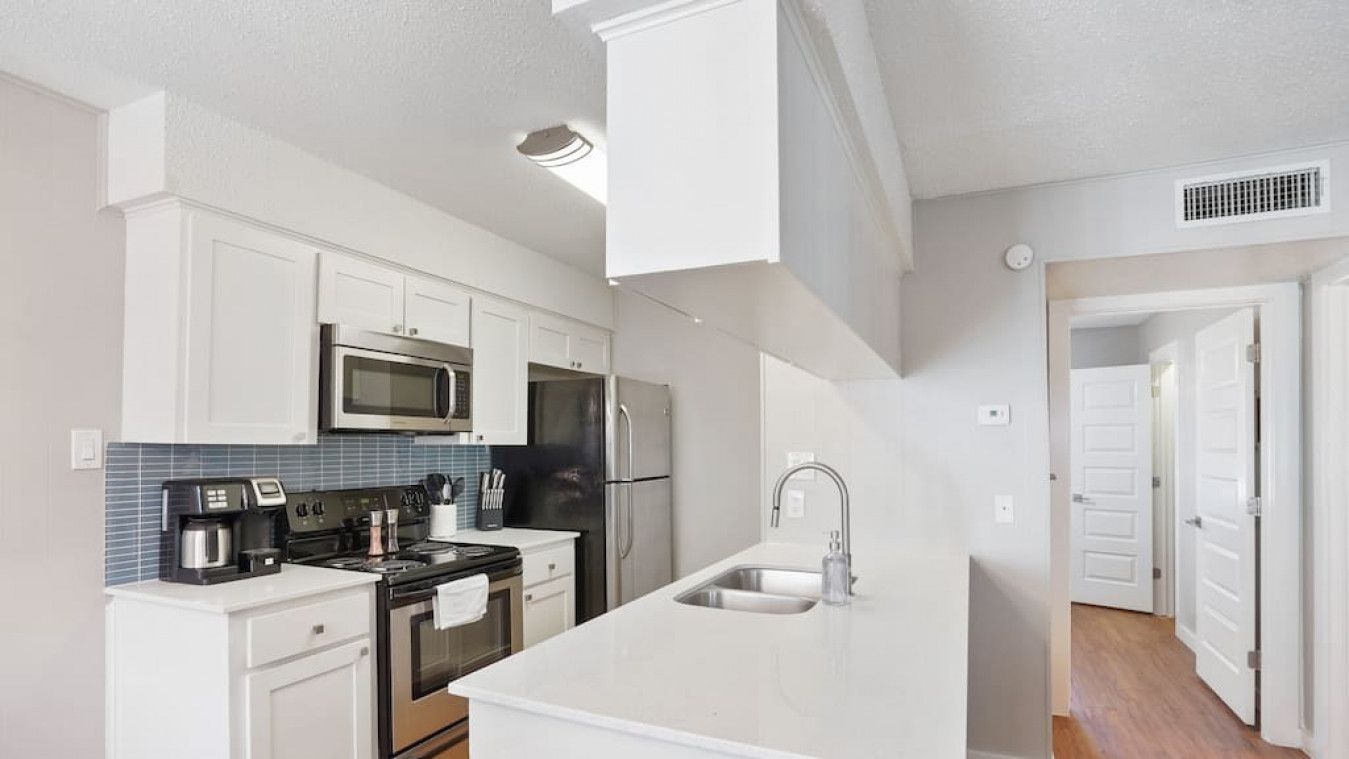 A modern kitchen with white cabinetry, a stainless steel refrigerator, a microwave, and a coffee maker.