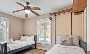 A bedroom with two beds, a ceiling fan, and windows with blinds.