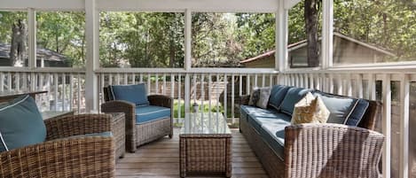 A covered porch with wicker furniture, a ceiling fan, and a view of the surrounding trees.