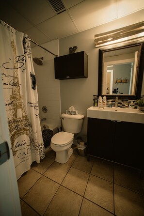 Et badeværelse med bruseforhæng med et Eiffeltårn-design, et toilet, en vask med toiletartikler og et spejl over vasken.