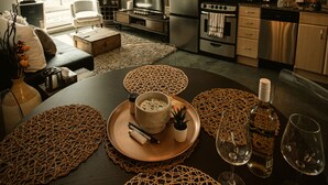 Et moderne køkken med rustfrie hårde hvidevarer, et spiseområde med vævede servietringe, og et hyggeligt opholdsområde med sofa og lænestol.