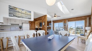 Cozinha moderna com detalhes em madeira, área de refeições com mesa grande e varanda com vista.