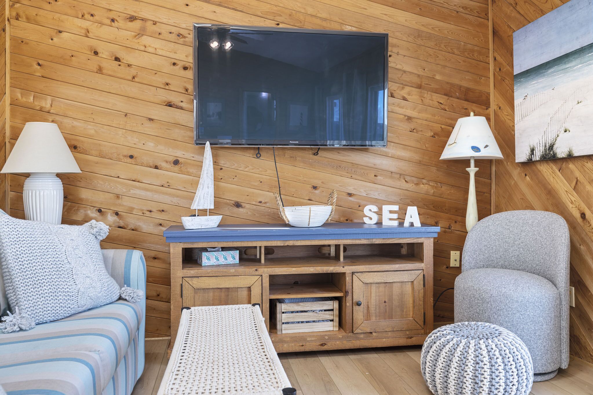 A cozy room with a wooden wall, a flat-screen TV, a sofa, a chair, and a small table with decorative items.