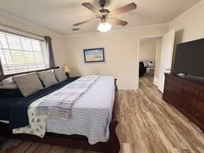 Une chambre à coucher avec un lit, un ventilateur de plafond, un tableau, une commode et un téléviseur.