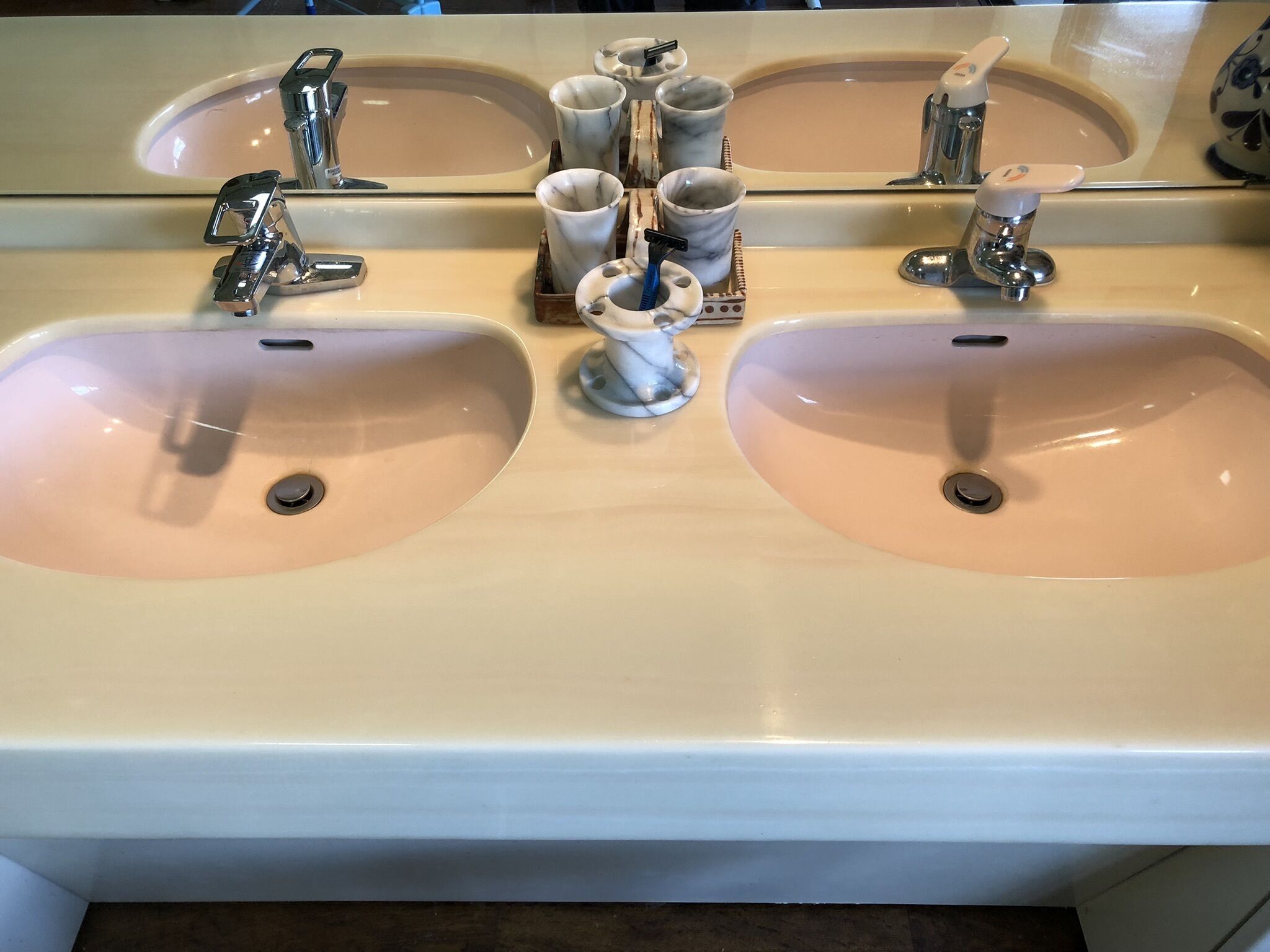 A bathroom with two sinks, each with a mirror above. There are multiple toothbrushes and a cup holder with cups and a toothbrush holder.