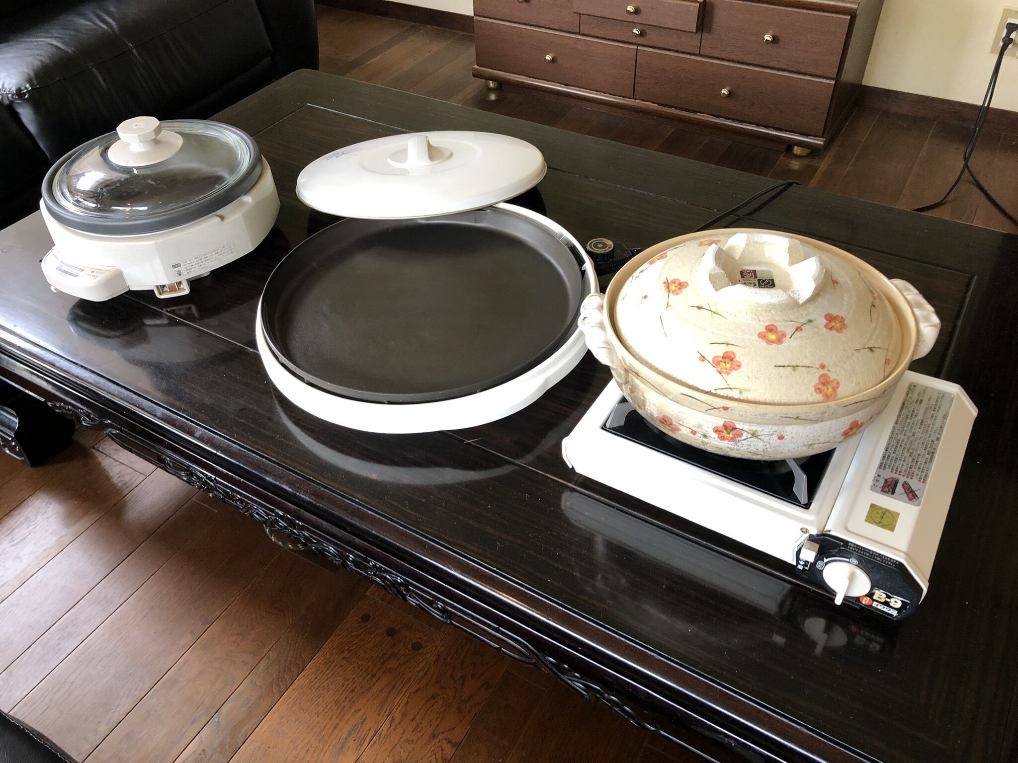 A kitchen counter with a rice cooker, a frying pan, and a pot on a portable stove.