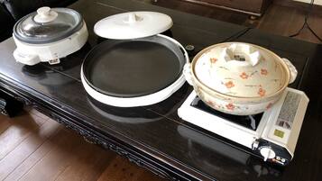 A kitchen counter with a rice cooker, a frying pan, and a pot on a portable stove.