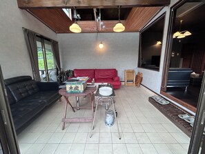 Una habitación con un sofá rojo, un sofá negro, una mesa de comedor con una caja, un taburete metálico y una ventana con cortinas.