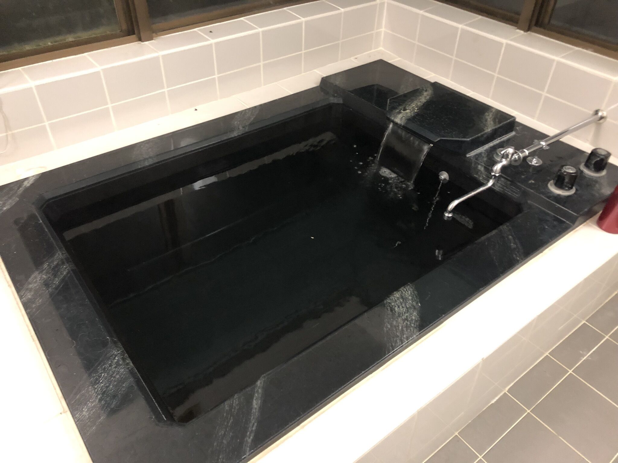 A black rectangular bathtub with a faucet and a handheld showerhead, set in a bathroom with white tiled walls.