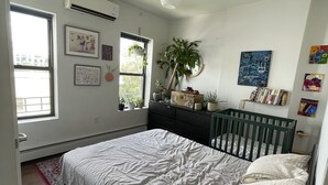 Un dormitorio con cama, cuna, ventana y varias decoraciones en las paredes.