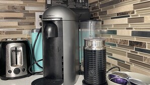 Una cocina con cafetera, tostadora, licuadora y un tazón de utensilios.