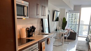 A modern kitchen with stainless steel appliances, a dining area with a glass table, and a view of high-rise buildings. - Perfect Studio 5 Icon Brickell Pool spa gym View (Miami)