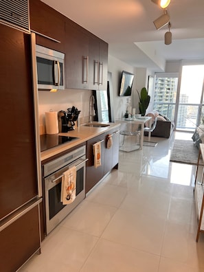 A modern kitchen with stainless steel appliances, a dining area with a glass table, and a view of high-rise buildings.