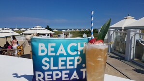 A beachside view with umbrellas, a drink with a straw and fruit, and a sign reading "BEACH SLEEP REPEAT".