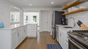 A modern kitchen with white cabinetry, a stainless steel refrigerator, a coffee maker, and a built-in stove.