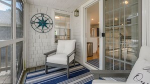 A cozy porch with a white chair, a blue and white striped rug, and a large window with a view into the house.