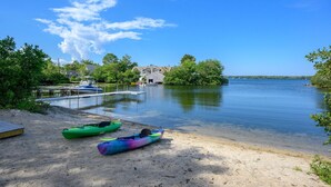 Une vue sur le lac, avec des kayaks sur le sable, une jetée avec un bateau, et des maisons en arrière-plan.
