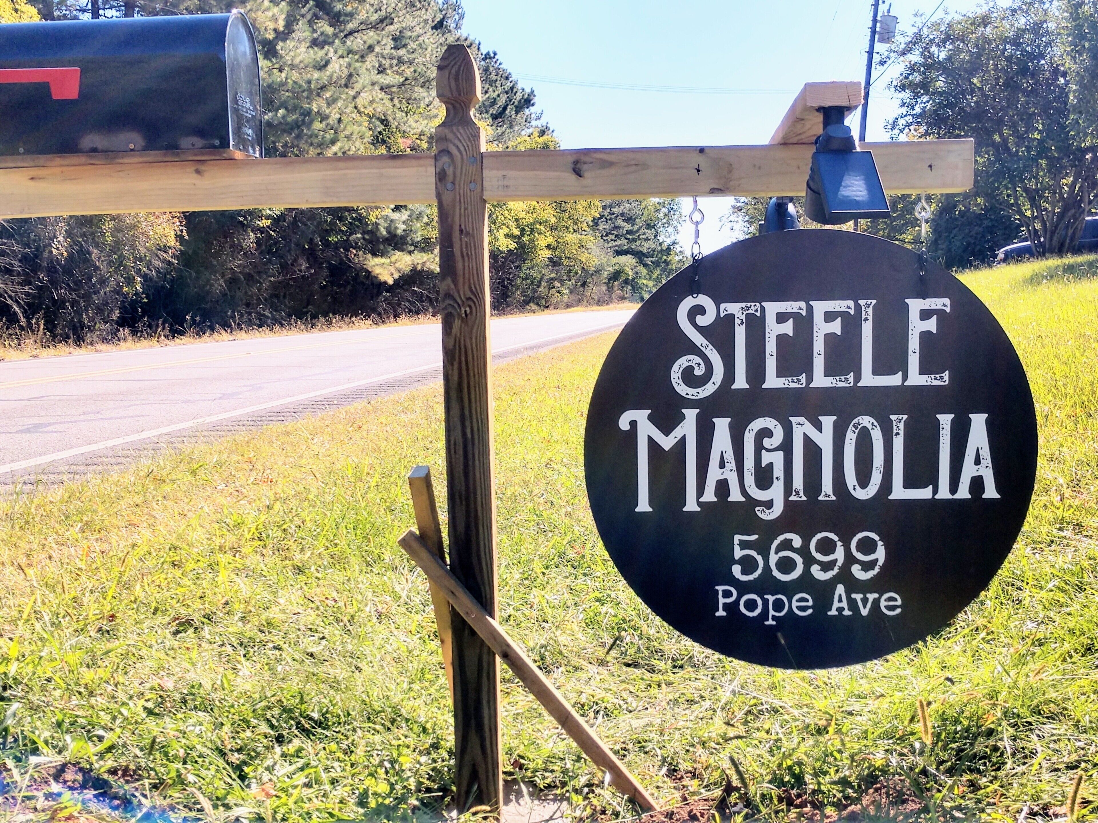 Un cartel con la inscripción 'STEELE MAGNOLIA 5699 POPE Ave' sujeto a un poste de madera.