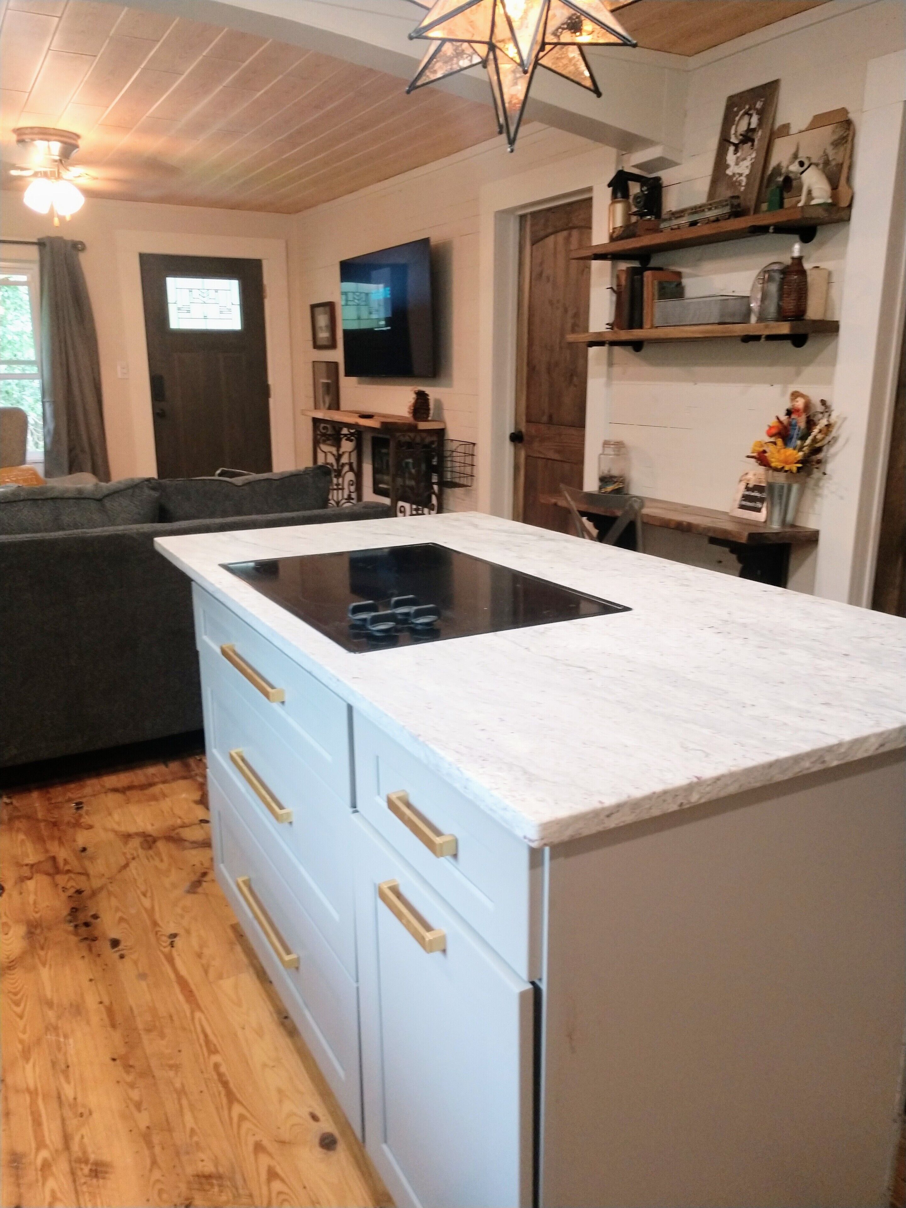 Una cucina moderna con piano cottura integrato, pavimento in legno e un divano grigioo nella zona soggiorno.
