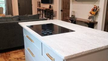 Una cucina moderna con piano cottura integrato, pavimento in legno e un divano grigioo nella zona soggiorno.