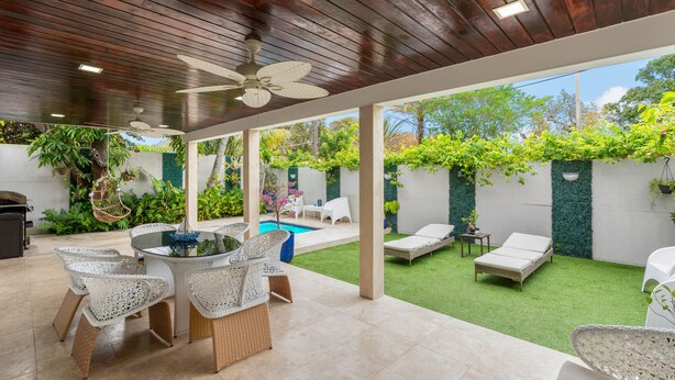 Ein überdachter Patio-Bereich mit Pool, Gartenmöbeln und üppiger Bepflanzung.