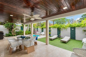 Un patio techado con piscina, mobiliario exterior y abundante vegetación.